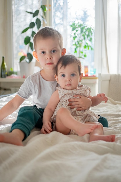 full length of sibling sitting on bed at home
