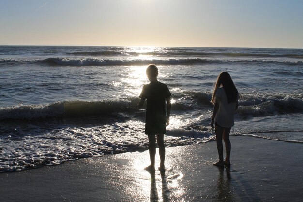 Photo full length of siblings standing on shore at beach against sky