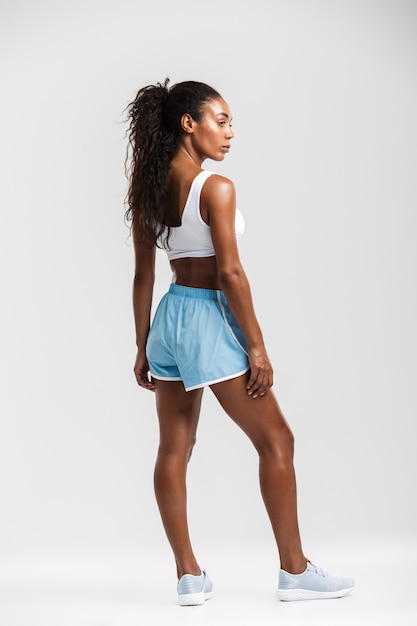 Full length side view of an attractive healthy confident african sportswoman standing isolated over white wall