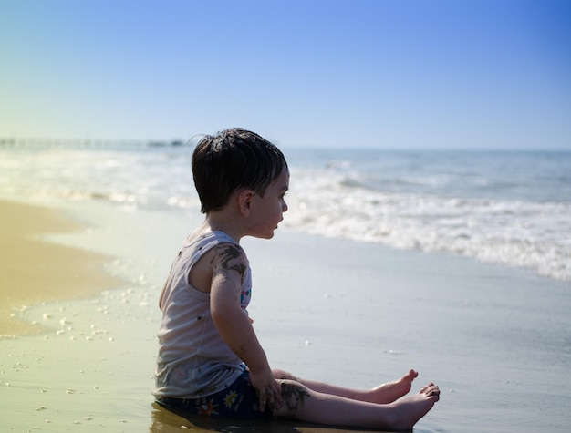 Photo full length side view of boy sitting on shore at beach