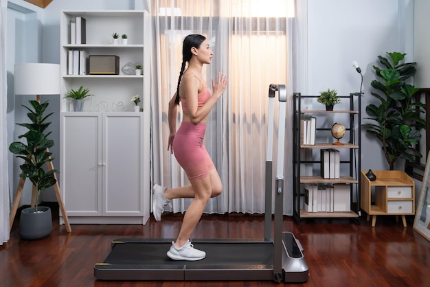 Photo full length side view of energetic and strong athletic asian woman running running machine at home pursuit of fit physique and commitment to healthy lifestyle with home workout and training vigorous