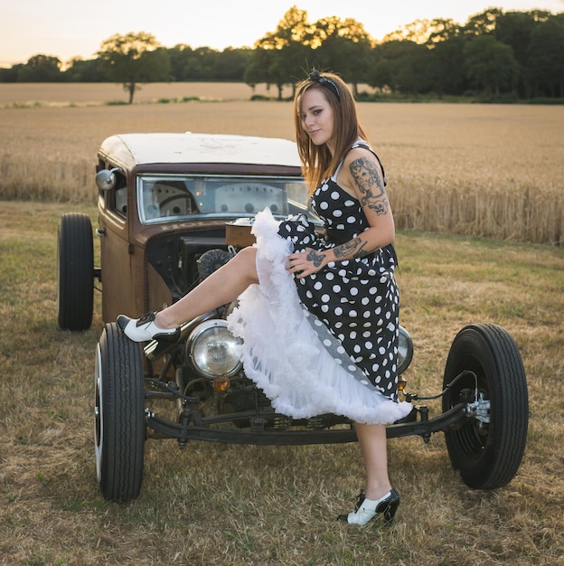 Photo full length side view portrait of tattooed young woman standing by vintage vehicle on field