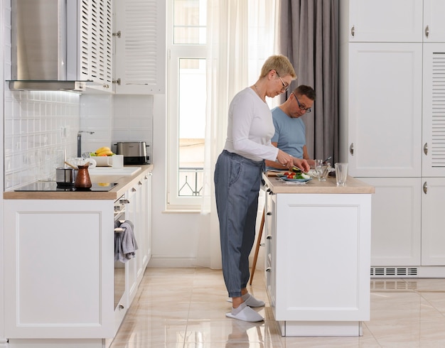 Full length side view senior couple cooking at the kitchen happy family portrait