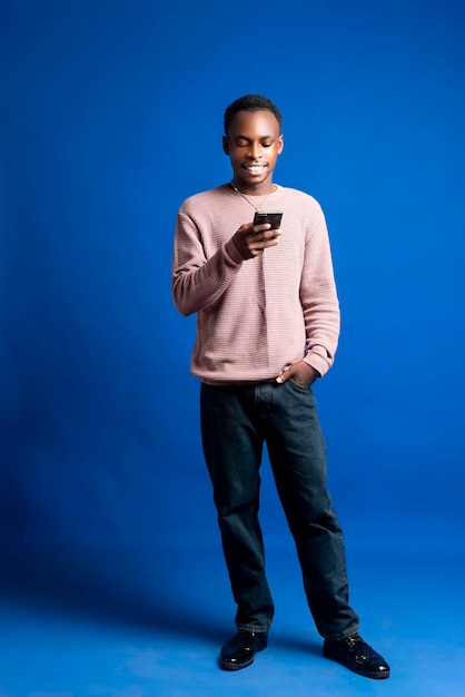 Foto vista laterale a tutta lunghezza di un giovane afroamericano sorridente di vent'anni che tiene in mano un telefono cellulare