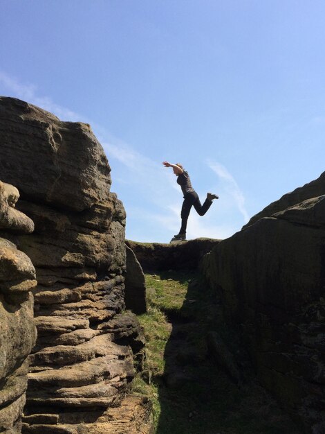 Photo full length side view of woman balancing on rock formation against sky at stanage edge