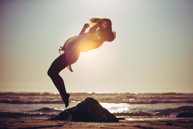 Foto vista laterale a tutta lunghezza di una donna che salta sulla spiaggia