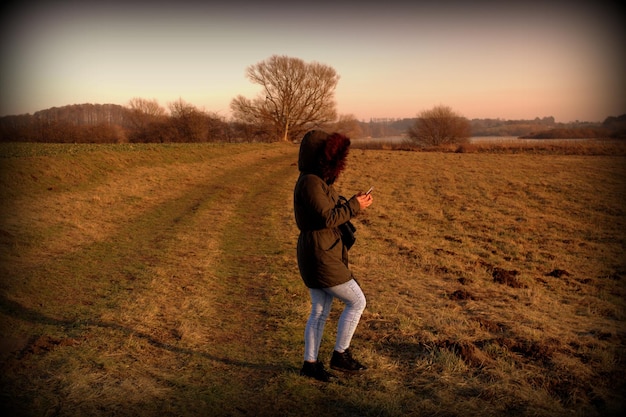 Full length side view of woman standing on field during sunset