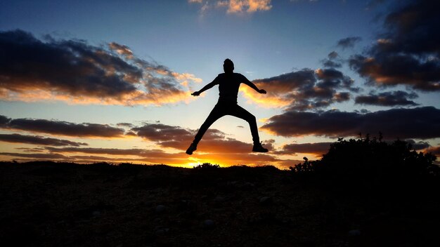 夕暮れの時に空に向かってジャンプするシルエット男の全長