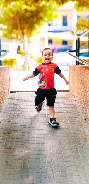 Photo full length of smiling boy running on footpath