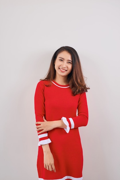 Полная длина улыбающейся игривой молодой женщины в красном платье, стоящей и смотрящей вверх на белом фоне