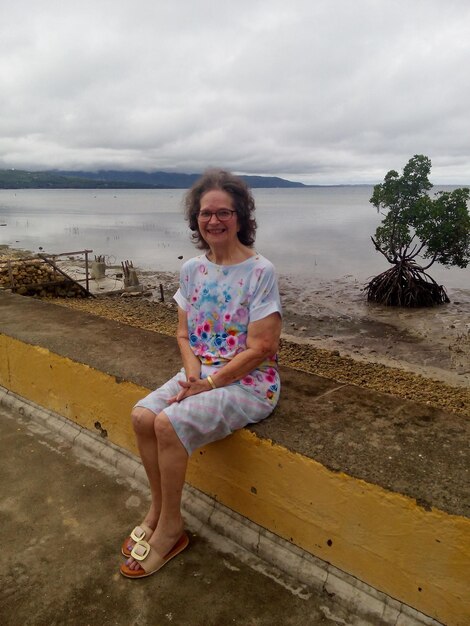 Full length of smiling senior woman sitting on beach