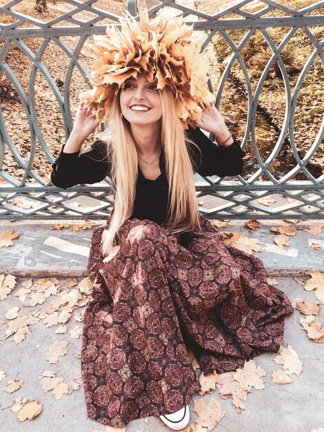 Photo full length of smiling woman with maple leaves sitting by fence