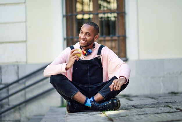full length of smiling young man holding apple while looking away in city