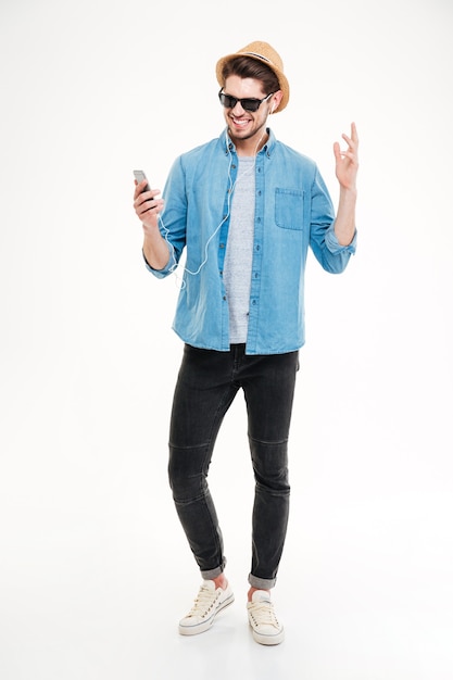 Full length of smiling young man listening to music from smartphone