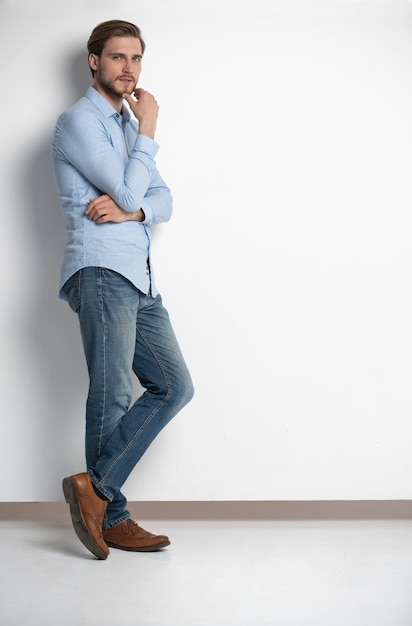 Full length studio portrait of casual young man in jeans and shirt smiling. Isolated on white background.