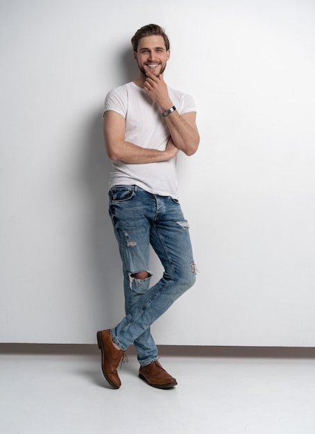 ジーンズとシャツの笑顔でカジュアルな若い男のフルレングスのスタジオポートレート。白い背景で隔離。