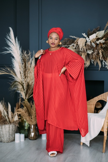 Full length studio shot of elegant charming African woman wearing bright red fashionable suit with traditional ethnic headwrap.