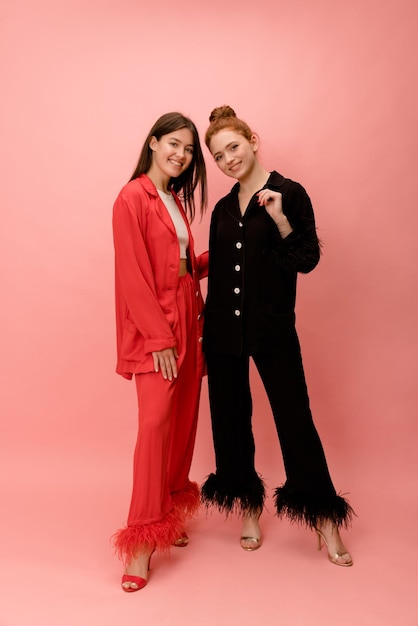 Full length stylish young caucasian ladies in red and black silk suit on pink background Elegant style spring fashion trends