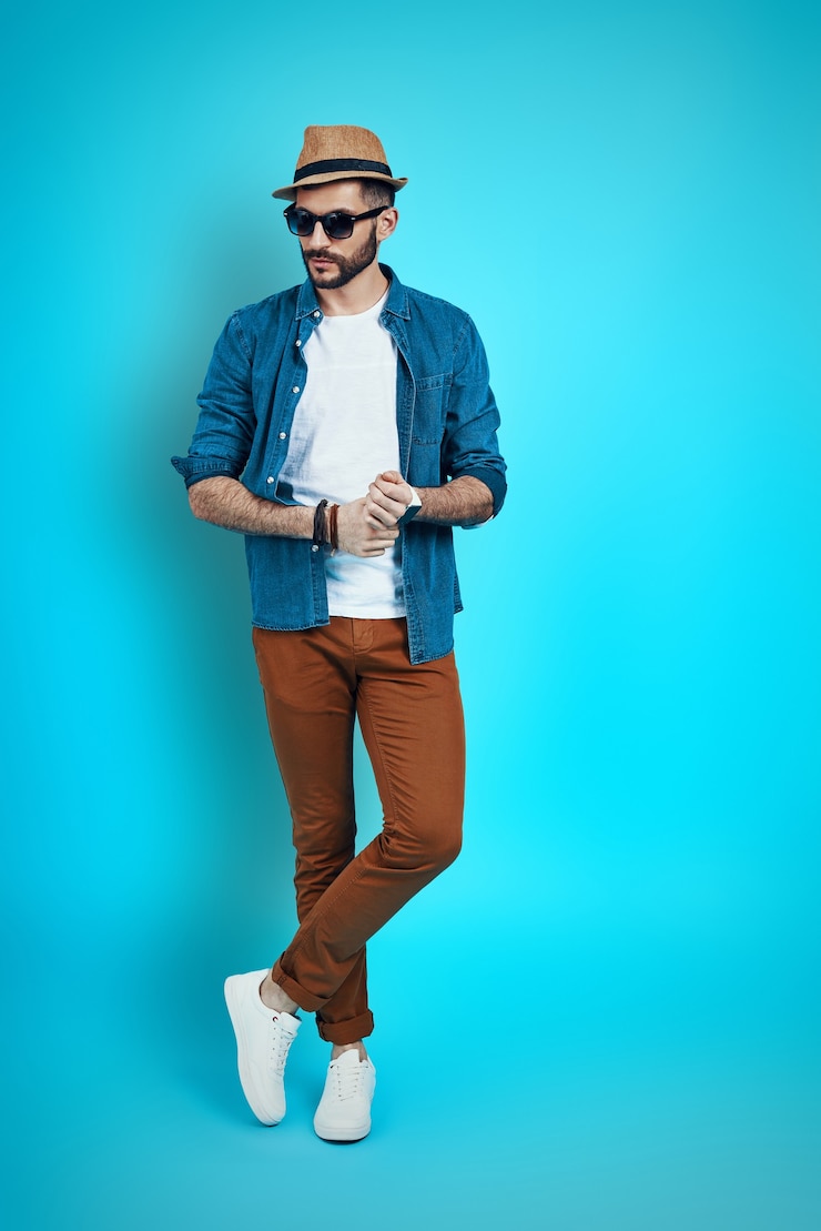 Photo full length of stylish young man wearing hat and looking away while standing against blue wall
