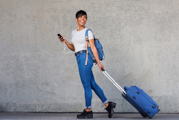 Full length traveling young woman with mobile phone and suitcase