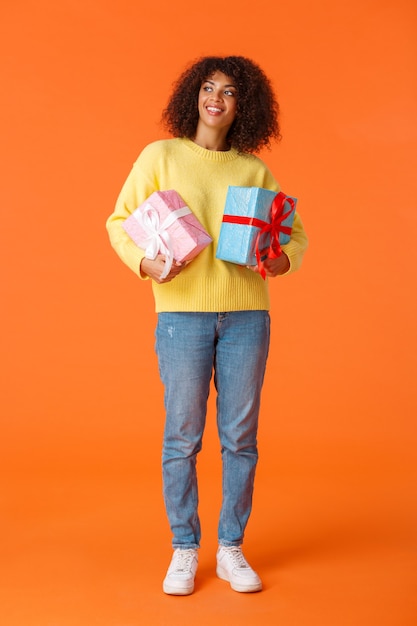 Full-length vertical shot dreamy and cute attractive african-american female looking around as going christmas, new year holiday party as secret santa