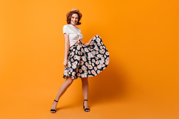 Full length view of adorable curly woman playing with skirt Pretty girl in summer outfit posing on yellow background