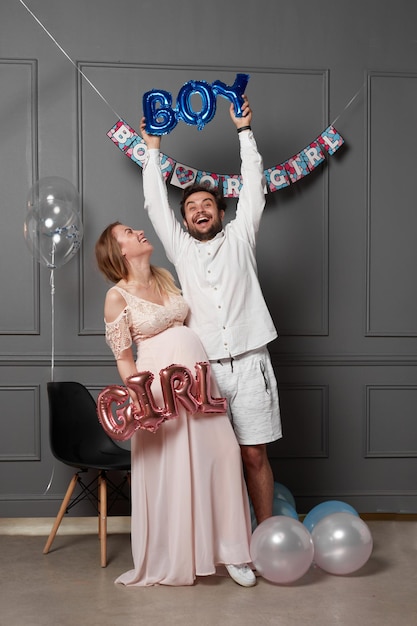 Full length view of a amused couple holding up inscription boy or girl during gender reveals party over balloons