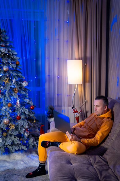 Full length view of the businessman wearing pajama sitting with the laptop near the fur tree A man is absorbed in working on his business