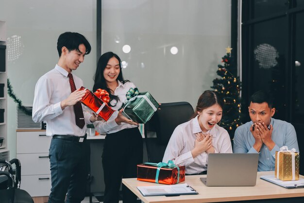 full length view of a group of business team wearing red Santa hat and exchange gift box together in the office for Christmas