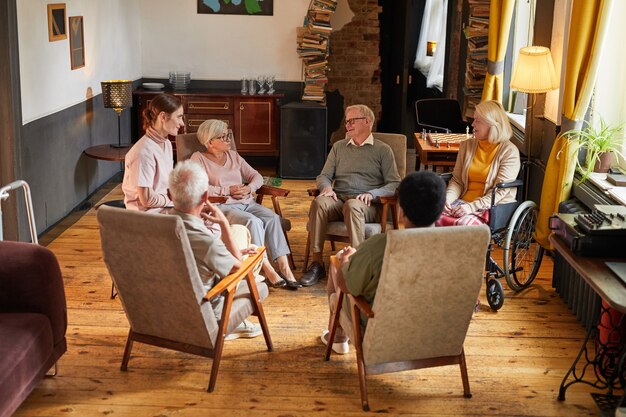 Foto vista a tutta lunghezza in un gruppo di persone anziane sedute in cerchio durante la sessione di terapia presso la casa di riposo, concentrarsi sulla donna che piange, copiare lo spazio