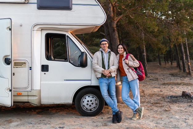 バックグラウンドで彼らの車でポーズをとっている間カメラを見ている愛情のあるカップルの完全な長さのビュー。ストック写真