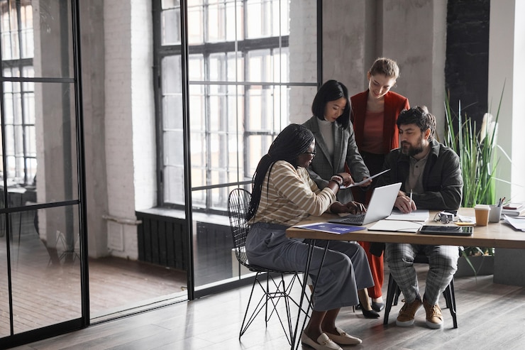 Photo full length view at multi-ethnic group of business people discussing project while sitting at meeting table in graphic office interior, copy space