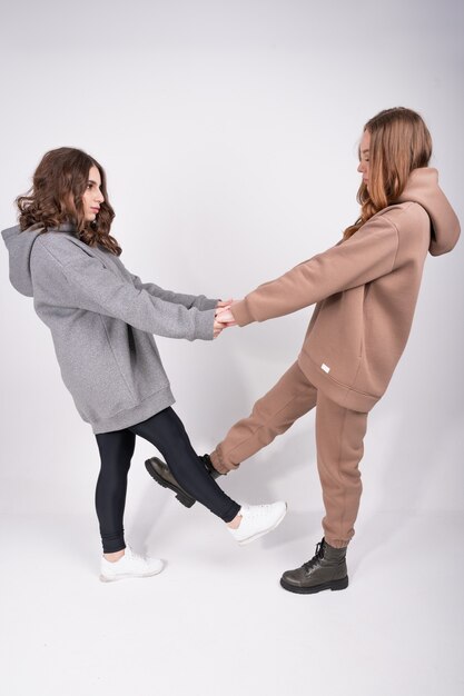 사진 트렌디 한 캐주얼 옷을 입은 두 젊고 세련된 소녀의 전체 길이보기는 손을 잡고 서로를 봅니다. 여성 캡슐 옷장 개념.