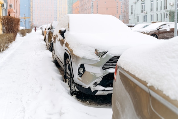 Вид в полный рост на ряд автомобилей под снегом после снегопада. Машины на заснеженной стоянке. Снежная зима и много снега