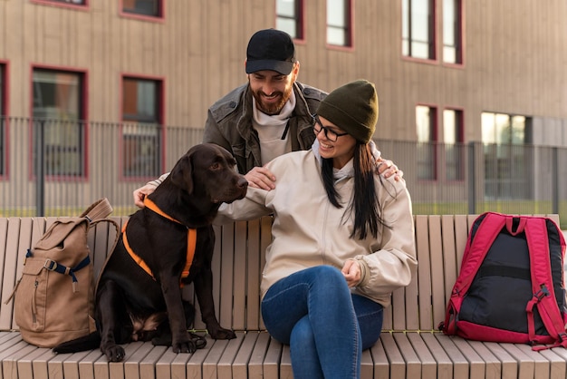 彼女の夫が彼女を抱きしめている間、ベンチで血統の犬を抱き締める笑顔のブルネットの女性の完全な長さのビュー。ペットケアのコンセプト