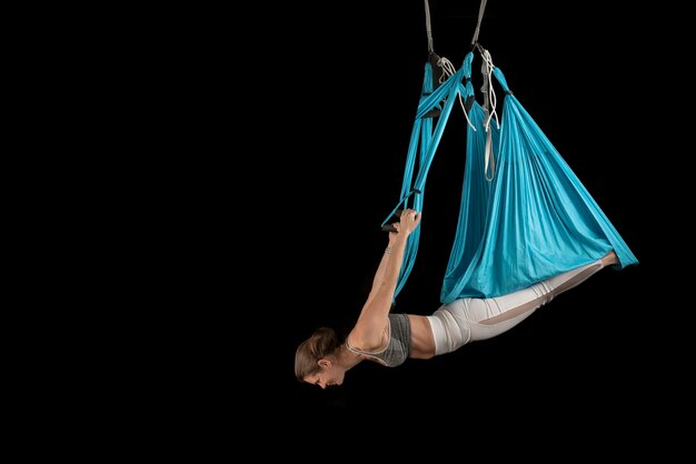 Full length view of the sport woman practices aero fly yoga position while hanging upside down Black background