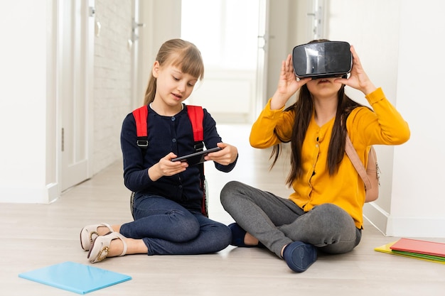 full length view of two multicultural schoolgirls holding hands while using virtial reality headsets on white background.