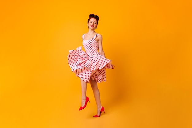 水玉模様のドレスを着た素晴らしい女性の全身像黄色の背景で踊る生姜の女の子のスタジオショット