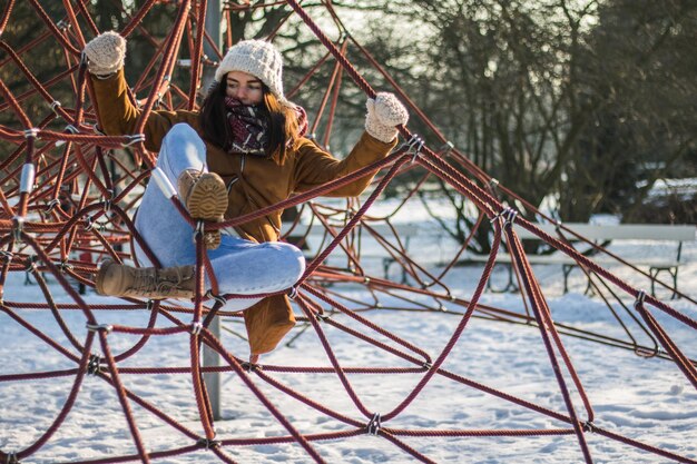 Foto lunghezza completa di una donna che si arrampica su corde in un parco coperto di neve