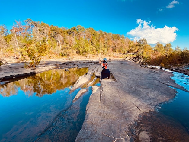 Foto lunghezza completa di una donna accovacciata vicino all'acqua nella foresta