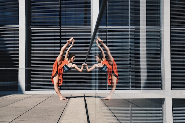 Foto lunghezza completa di donna che fa ginnastica sul pavimento con riflesso nella finestra di vetro dell'edificio