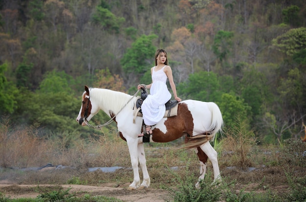 Full Length Of Woman on dress riding Horse On Field By Trees Against Sky