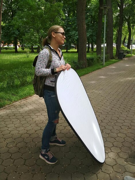 Full length of woman holding reflector while standing on footpath in park