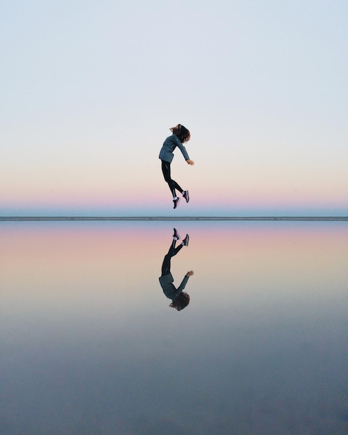 full length of woman jumping on beach against sky during sunset