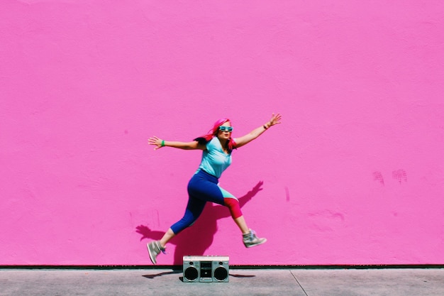 Foto lunghezza piena di donna che salta su una radio antiquata contro un muro rosa