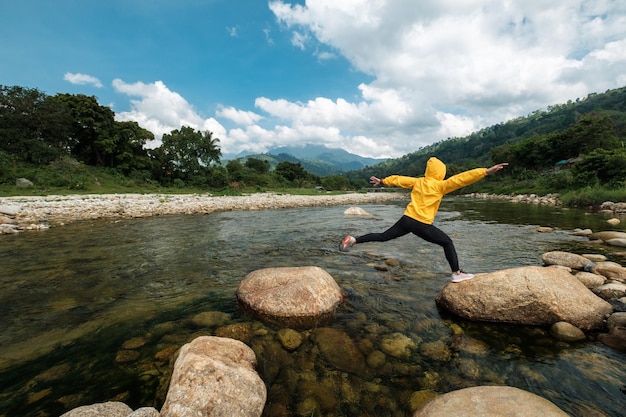 Foto lunghezza completa di una donna che salta sul fiume su una roccia