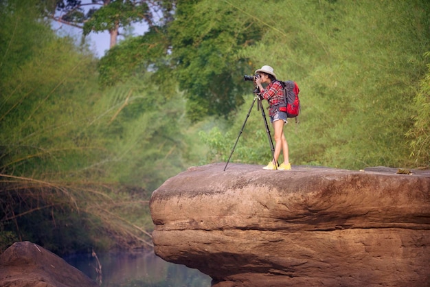 Full length of woman photographing while standing on rock against trees