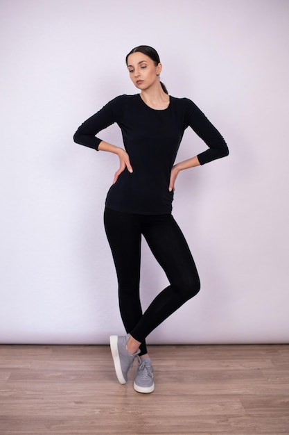 白い背景の人にスタジオで黒い緊密な服とスニーカーでポーズをとる全身の女性