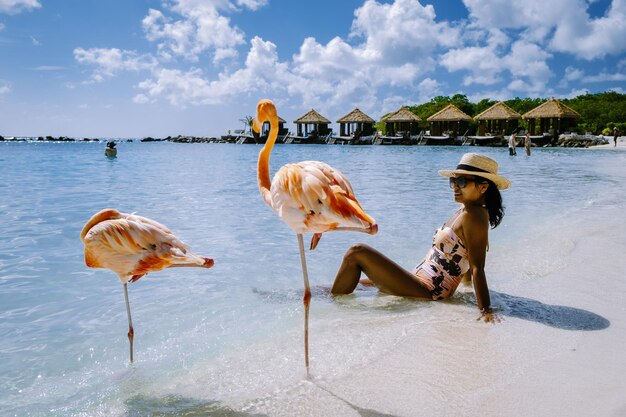 Foto lunghezza piena di donna seduta sulla spiaggia con i fenicotteri