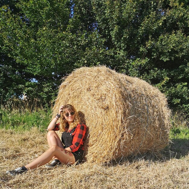 Foto lunghezza completa di una donna seduta da una palla di fieno contro un albero